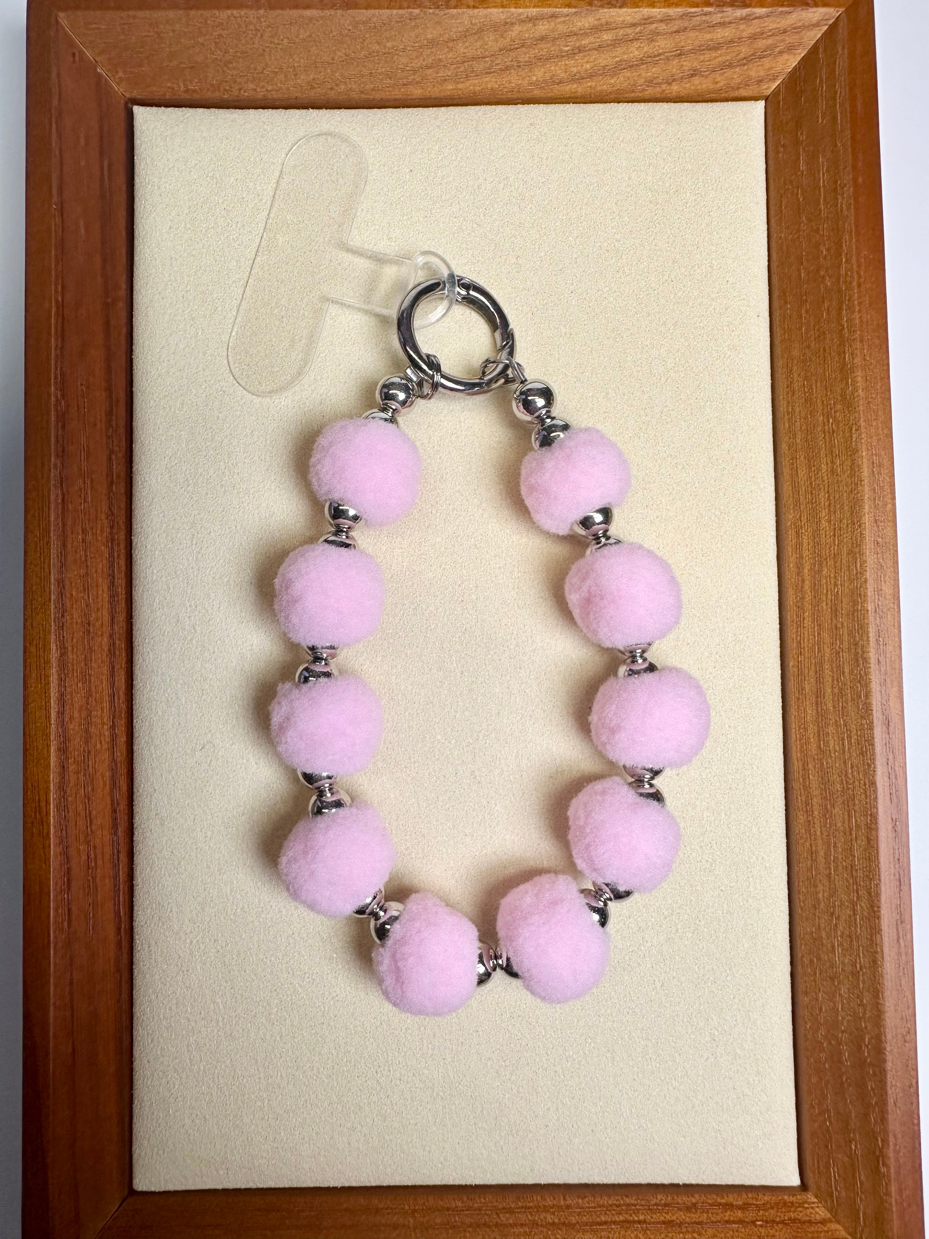 Pink fuzzy beaded phone charm on a beige card with a wooden frame