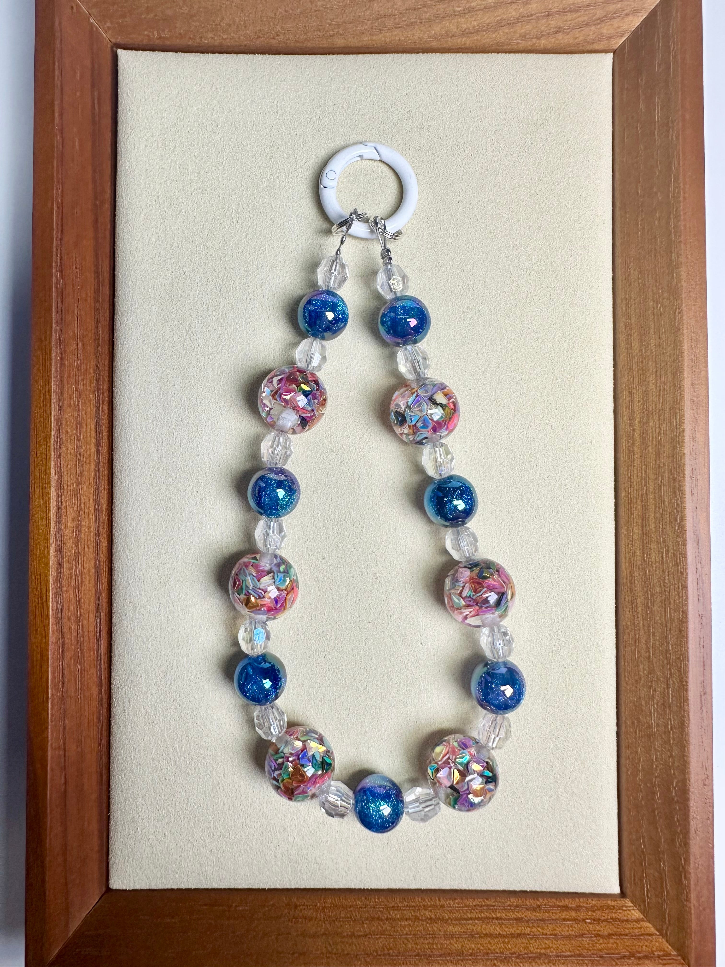 Beaded phone charm with blue and clear and colorful confetti beads on a beige background