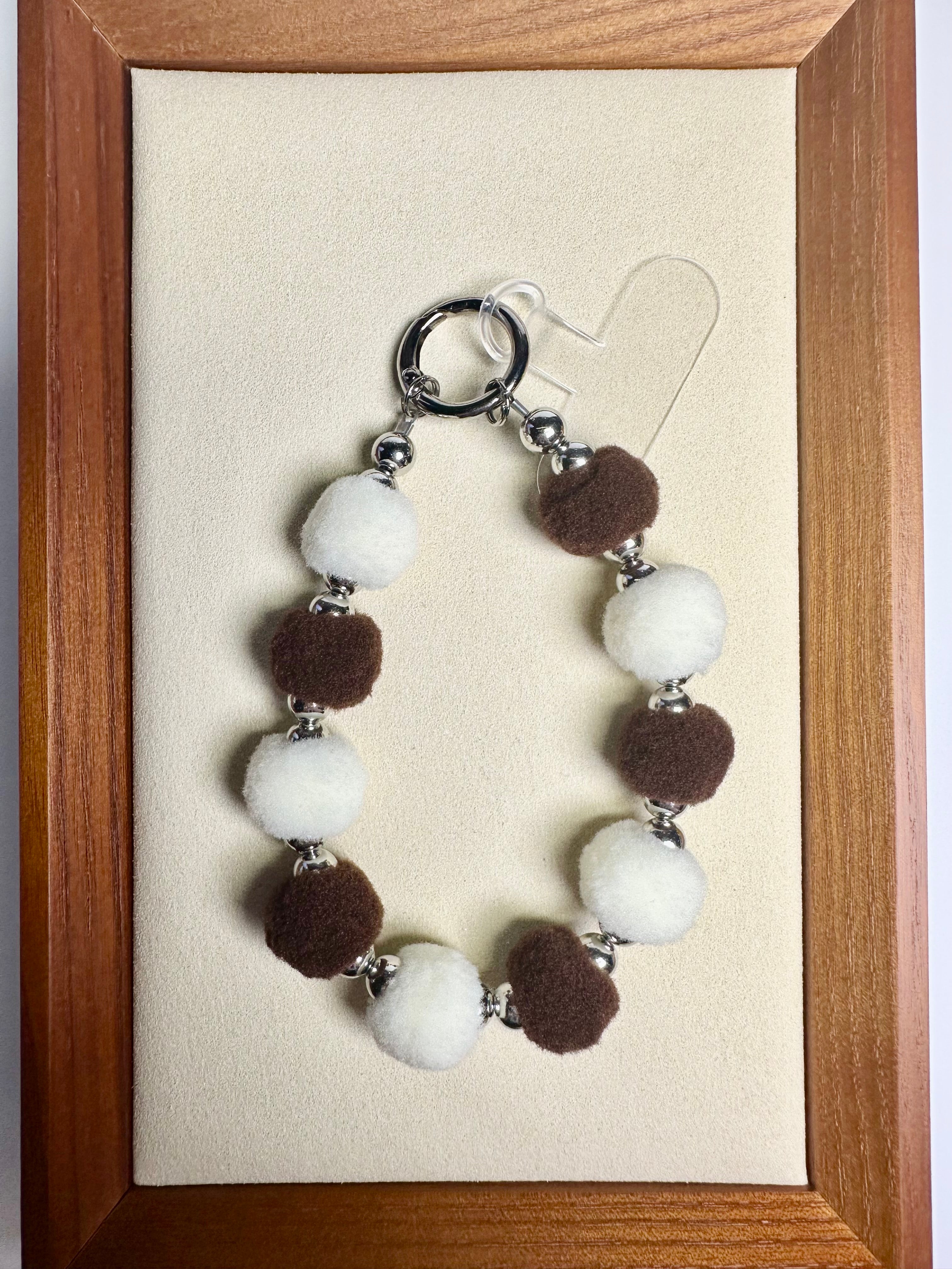 phone charm with fuzzy brown and beige beads on a beige card, framed in wood.