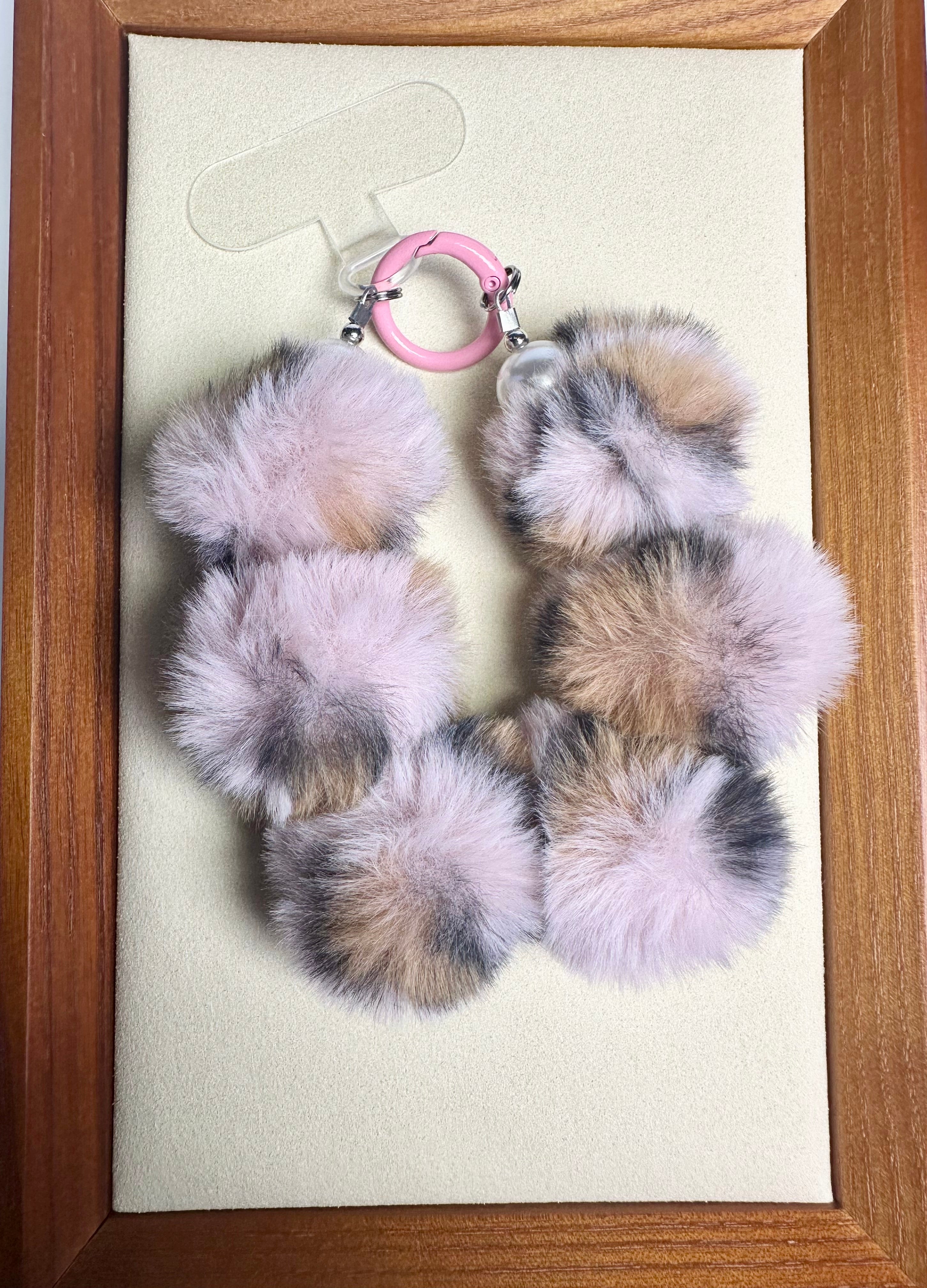 Furry pink & brown phone charm with pink ring on a beige card inside a wooden frame
