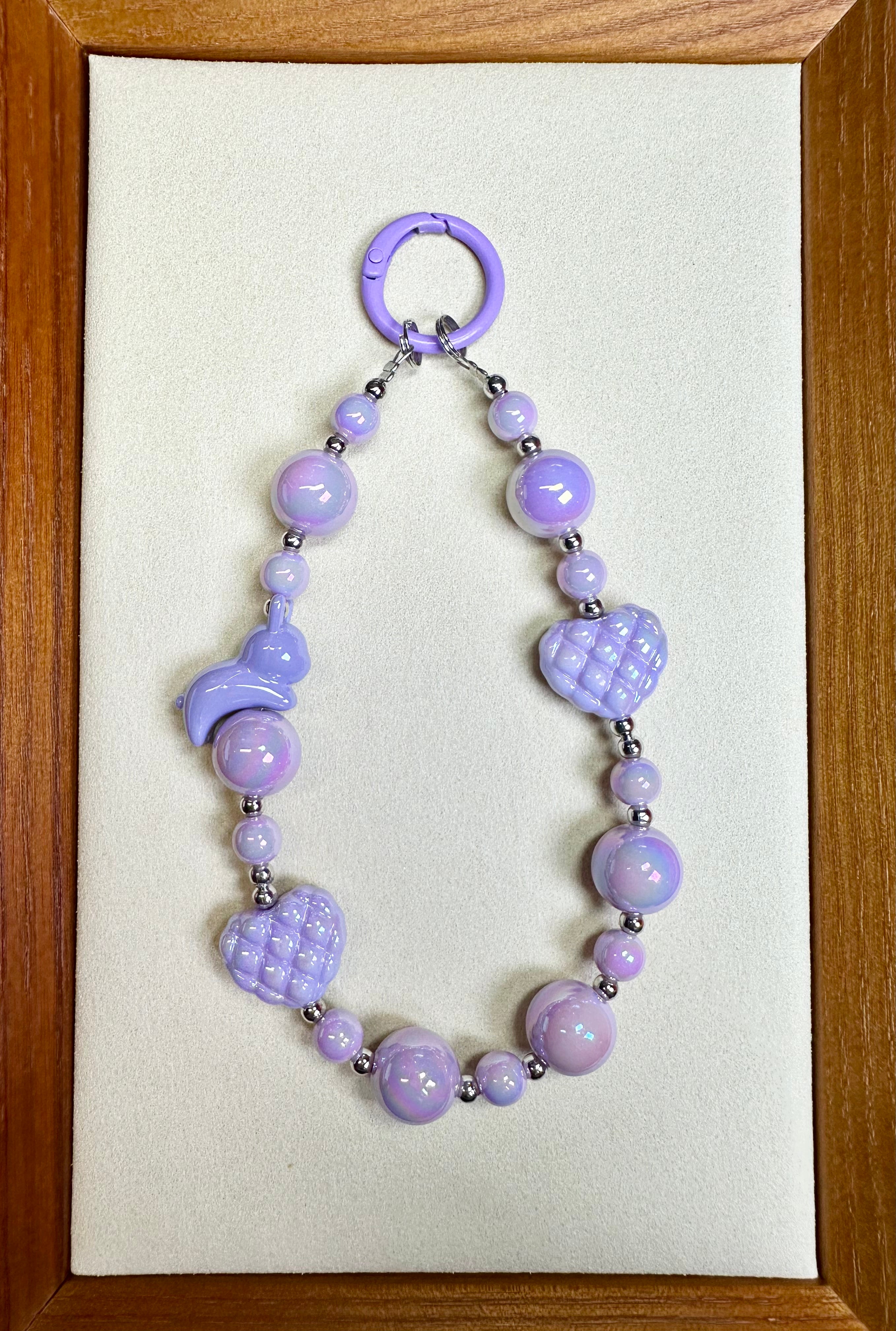 Purple beaded phone charm on a beige card with a wooden frame