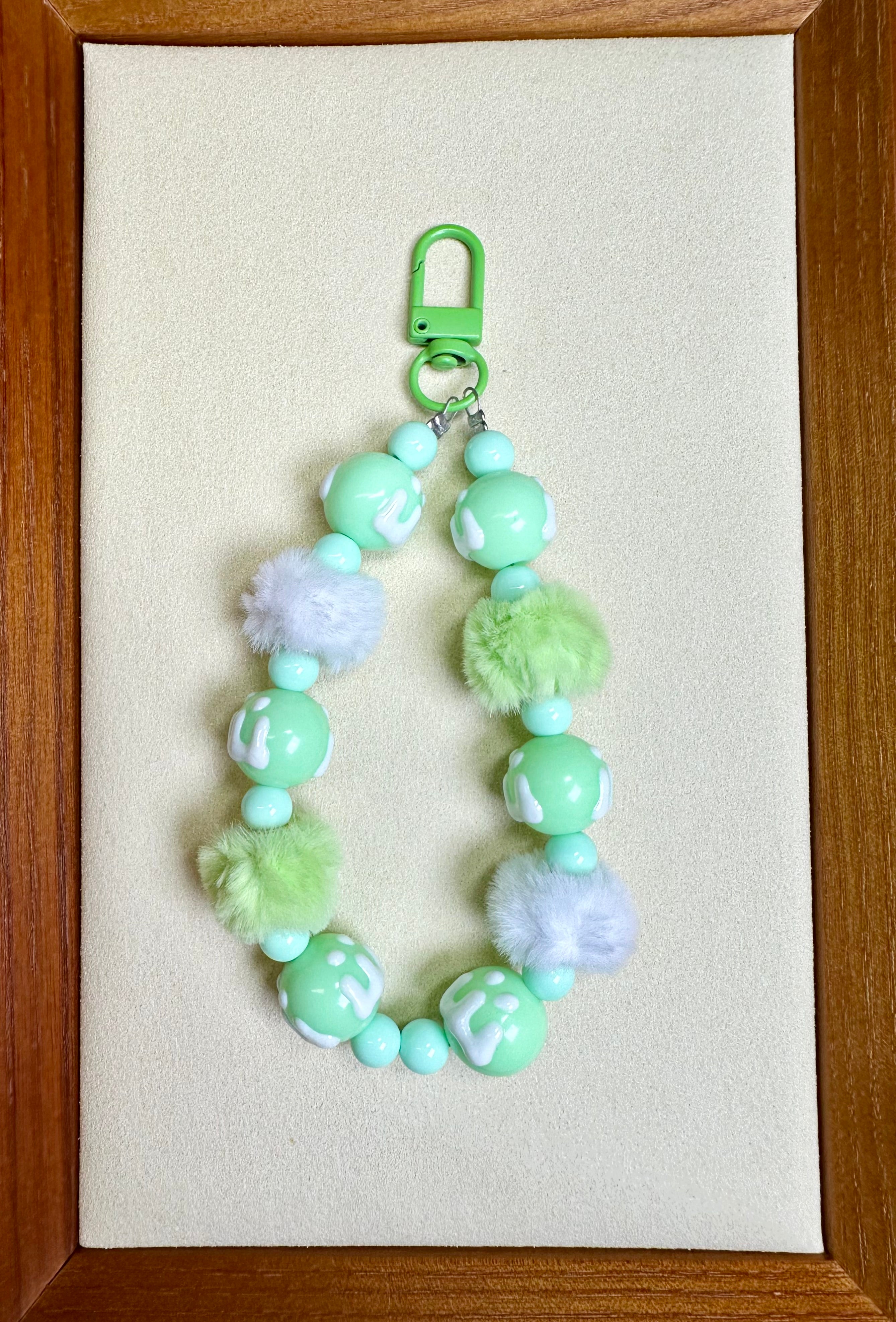 Green beaded phone charm on a beige background