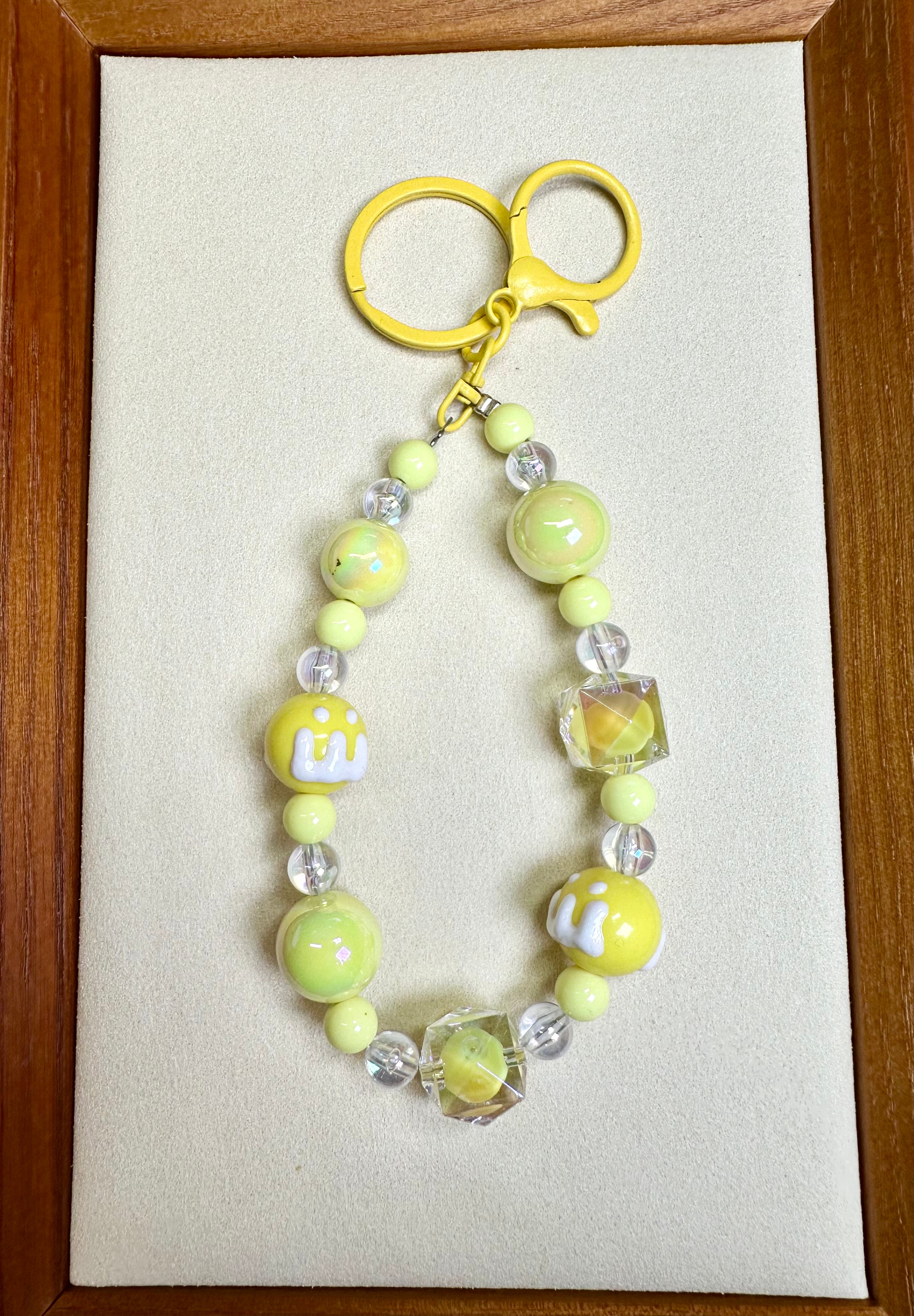 Yellow beaded phone charm on a beige card with a wooden frame